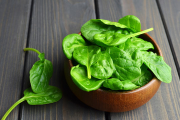 Fresh spinach leaves in wooden bowl over old wooden table. Healthy vegan food. Green living and eco-conscious concept.