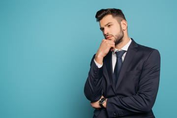 thoughtful businessman holding hand near face on blue background