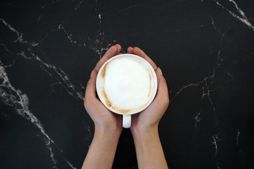 hands holding a cup of coffee, with black marble background