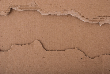 Old textured cardboard sheet with torn edges. Brown cardboard torn off. Cardboard texture. A sheet of tattered cardboard lies on a whole sheet of cardboard