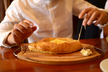  Khachapuri in Adjarian. Close-up. Children's Hands stretch the melted cheese. Homemade Georgian food in a restaurant. Delicious food delivery. National food. Good quality photos. Copy space
