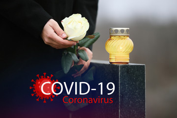 Funeral ceremony devoted to coronavirus victims. Woman holding rose near tombstone with candle...