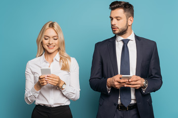 smiling businesswoman and curious businessman using smartphones on blue background