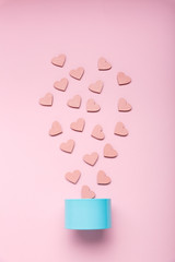 Blue little metal gift box and pink decorative hearts that fall out of it on a pink background.
