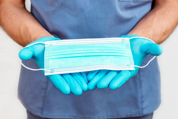 Medical doctor wearing scrubs and gloves, holding a protective face mask flat on his hands