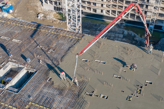 Pouring cement on the floors of residential multi-story building under construction using a concrete pump truck with high boom to supply the mixture to the upper floors. Aerial high top drone view.