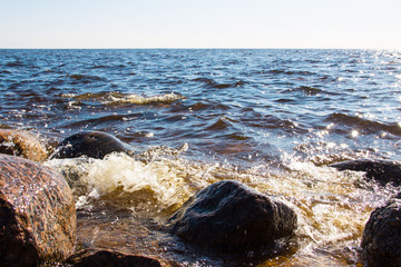 Sea background. Sea stones and surf, the wave hits the rocks. Sea water surface lit by sunny light. Summer sunny sea water scene. Nature concept. Beautiful summer landscape. Vacation concept.