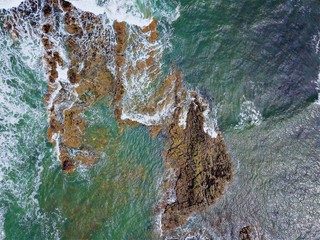 Aerial drone view looking down, bird's eye perspective. Ocean waves crash off coastal rocks near...