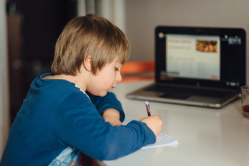 Kid studying online writing in his notebook. Studying home