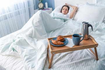 Young woman with her Breakfast in bed - croissant with a cup of coffee.