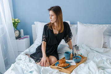 Happy young beautiful woman have breakfast in bed in her bedroom at morning