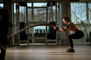 Young woman with battle ropes exercise in the fitness gym