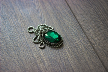A beautiful emerald pendant lies on a natural dark wooden cover