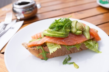 Fetta di pane con fette di salmone, e avocado decorata con la  rucola servita su un piatto