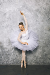 Fototapeta premium Pretty young ballerina dancer dancing classical ballet against rustic wall
