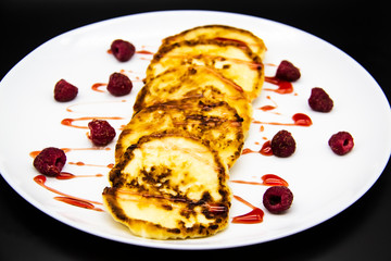 Ukrainian cottage cheese fritters, syrniki with jam on white plate. Cheese pancakes with raspberry without GMO. Delicious breakfast food at the morning.
