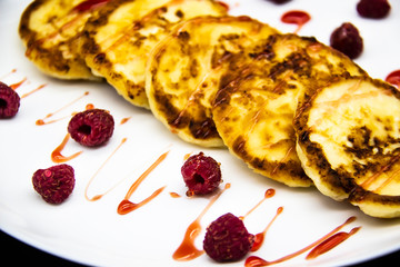 Ukrainian cottage cheese fritters, syrniki with jam on white plate. Cheese pancakes with raspberry without GMO. Delicious breakfast food at the morning.