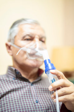 Senior man using medical equipment for inhalation with respiratory mask, nebulizer