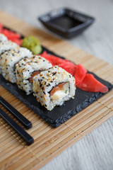 Sushi roll with seafood and soy sauce, wasabi and ginger. Sushi roll on a black board.