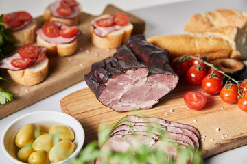 selective focus of tasty ham on cutting board with cherry tomatoes, olives and baguette near canape