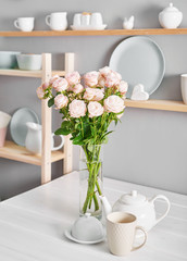 Utensils, bouquet of roses and mugs on shelf. Dishes in cupboard in kitchen.
