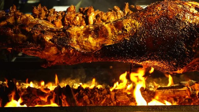 Grilled roasted lamb barbecue spinning on spit in wood fire