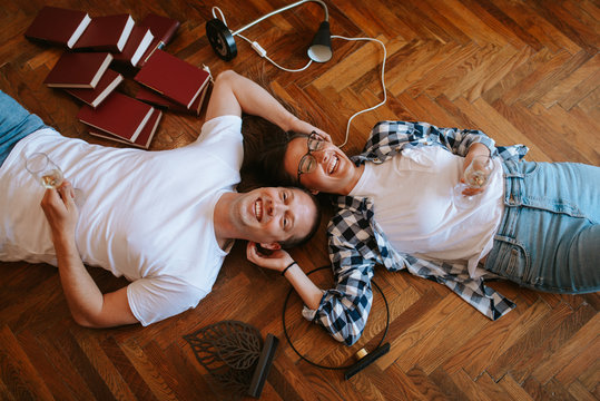Acaucasian boyfriend and a girlfriend are celebrating moving into a new apartment. Loving couple lying on the floor drinking wine