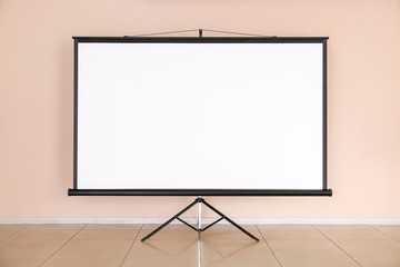 Modern projector screen near wall indoors