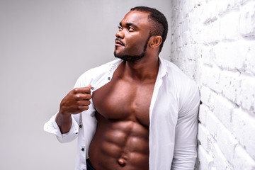 Obraz na płótnie Canvas Strong african athlete in a white shirt. Posing showing perfect muscle shape near a white brick wall