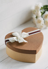 Beautiful brown gift box in the form of heart with a bouquet of flowers on the background