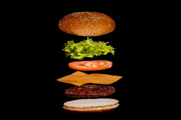 Flying ingredients burger or cheeseburger on a small wooden cutting board isolated on a dark background. Burger floating in the air above the table. Space for text
