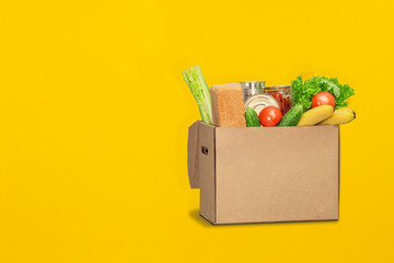 Donation box with food on a yellow background. Coronavirus food delivery. Volunteer brings a box of food. Donation, quarantine concept. Volunteer collecting food. Copyspace.