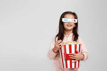 beautiful caucasian child girl wearing red-blue 3d glasses and eating popcorn from bucket isolated on gray background. copy space