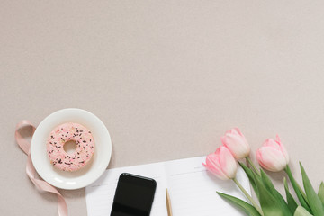 flat lay blogger or freelancer with delicate pink tulips, office supplies, Donat and phone on a coffee dusty background with copy space