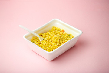 Instant noodles on a pink minimal background in a plastic box. Fast food and junk food concept. Creative minimal concept.
