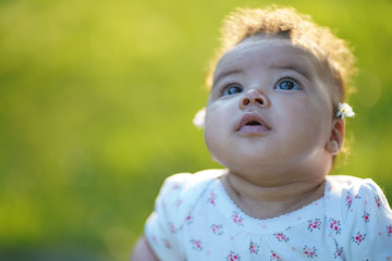 beautiful baby portrait looking up to the sky during sunset wearing 4 months to 6 month baby suit. Green grass backgrounds and sun that comes from the back of the baby. 85mm lens photography