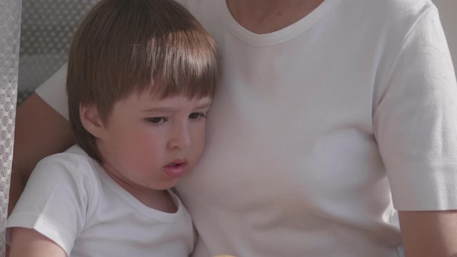Woman sits on window sill with cute toddler boy on her knees. Lockdown quarantine because of coronavirus COVID19. Self isolation at home. 10bit V-logL
