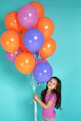 Smiling little child girl in pink t-shirt posing with bright colorful air balloons isolated on blue background. birthday party.