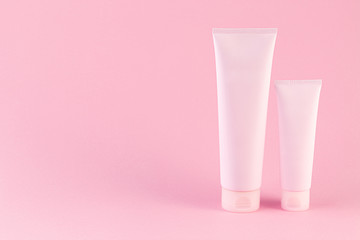 Two cosmetic tubes package on pastel pink background. Blank plastic containers, simple packaging...
