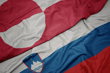 waving colorful flag of slovenia and national flag of greenland.