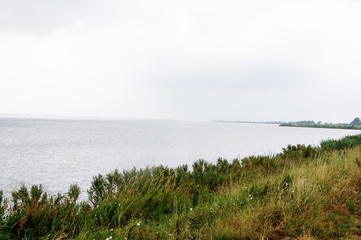 Rainy weather on the sea, where the coastline with green grass is visible