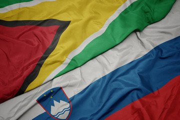 waving colorful flag of slovenia and national flag of guyana.