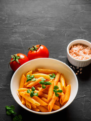 Pasta Penne in tomato sauce Pomodoro, garnished green basil leaves on black table. Traditional italian food. Copy space