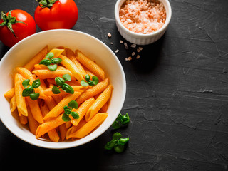 Pasta Penne in tomato sauce Pomodoro, garnished green basil leaves on black table. Traditional italian food. Copy space, top view