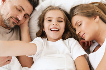 Photo of girl taking selfie photo while lying with sleeping parents