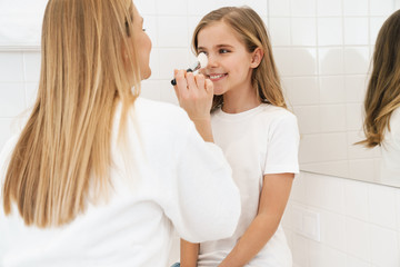 Obraz na płótnie Canvas Photo of mother and daughter smiling while doing makeup in bathroom