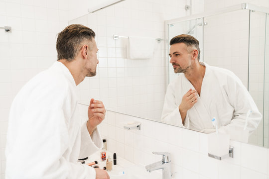 Photo of man holding toothbrush and looking at mirror in bathroom