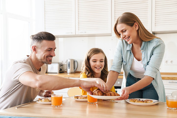Obraz na płótnie Canvas Photo of happy family eating croissants while having breakfast