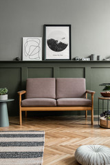 Stylish interior of living room with brown wooden sofa, design furnitures, plants, pillow, elegant accessories, green wood panelling with shelf and mock poster frames in modern home decor. 