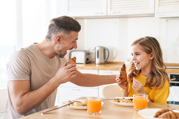 Photo of father and daughter laughing while having breakfast in kitchen